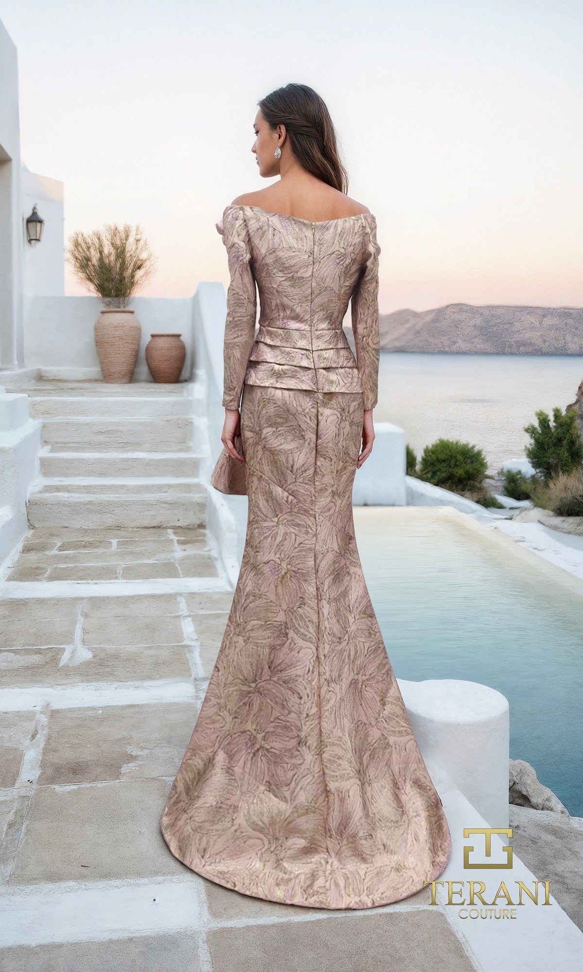 A woman stands outdoors beside a pool, facing away, wearing the Long Formal Dress: Terani 261M6448. The elegant mother-of-the-bride setting is enhanced by terracotta pots and a coastal landscape.